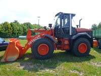 Orangefarbener Radlader mit breiter Schaufel auf einer Wiese
