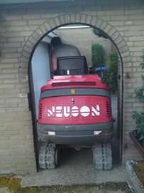 Roter Minibagger von hinten, eingefahren in einen schmalen gemauerten Rundbogen