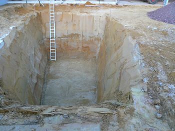 Tief ausgehobene Grube mit senkrechten Sandwänden und eingestellter Leiter