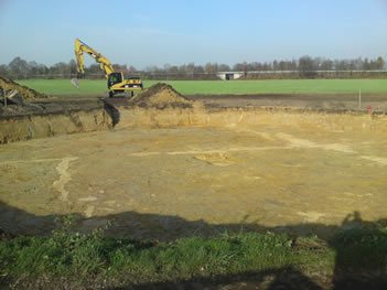 Kettenbagger am Rand einer großflächigen Baugrube auf einem Feld