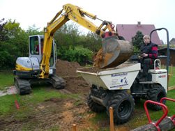 Minibagger belädt einen Minidumper mit Erde in einem Garten