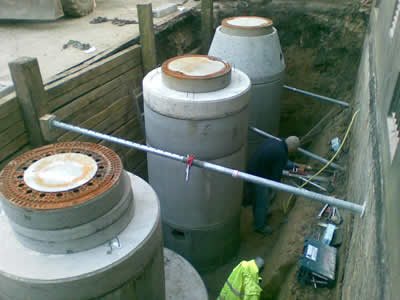 Mehrere gesetzte Betonschächte in einem verbauten Graben, ein Arbeiter daneben