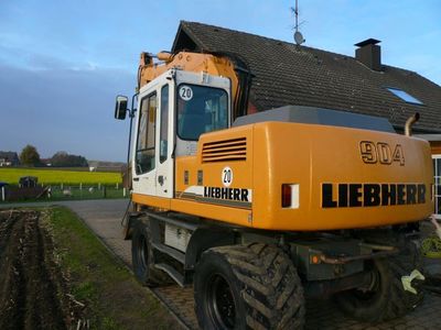 Liebherr-Mobilbagger 904 in Orange und Weiß auf einer Hofeinfahrt vor einem Wohnhaus