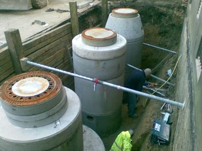 Mehrere Betonschächte in einer mit Holzbohlen verbauten Grube, ein Arbeiter in Warnkleidung dazwischen