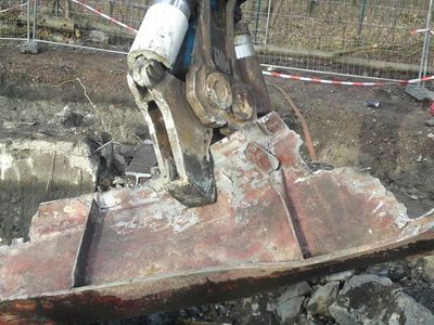 Abbruchzange am Bagger hält ein verbogenes, rostiges Stahlteil über Betonschutt