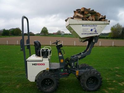 Weißer Minidumper HD1000 mit hochgefahrener Mulde voller Brennholz auf einer Wiese