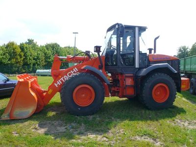 Orangefarbener Hitachi-Radlader mit Schaufel auf einer Wiese