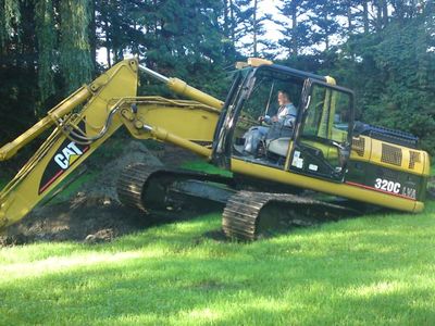 CAT-Kettenbagger 320C mit Fahrer in der Kabine auf einer Rasenfläche