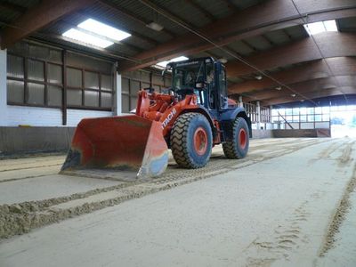 Hitachi-Radlader zieht Spuren in den Sandboden einer Reithalle