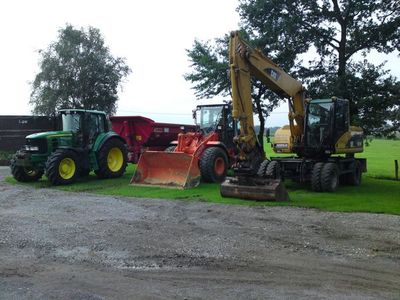 Maschinenpark auf einem Hof: Traktor mit Anhänger, Radlader und Mobilbagger nebeneinander auf Rasen