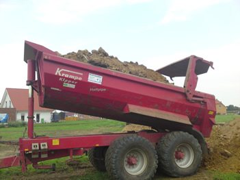 Roter Kipperanhänger mit halbrunder Mulde, beladen mit Erdreich