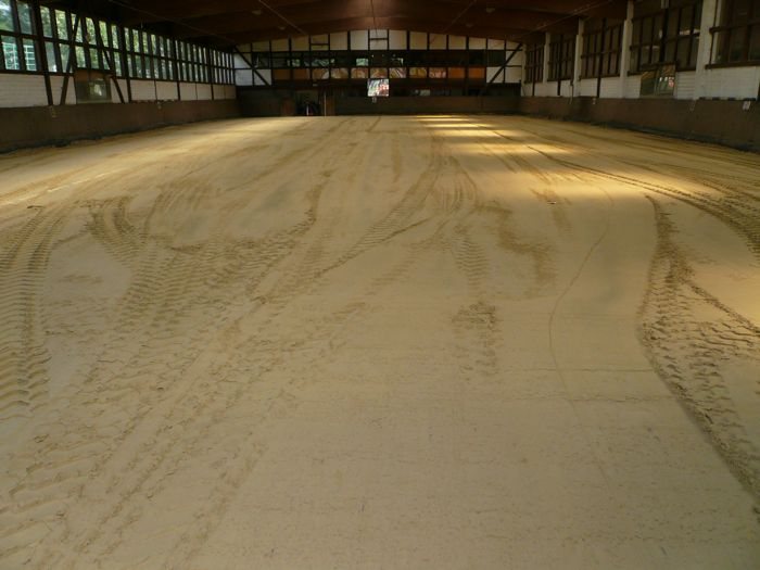 Hallenboden aus hellem Sand mit Reifenspuren, Blick über die leere Reithalle